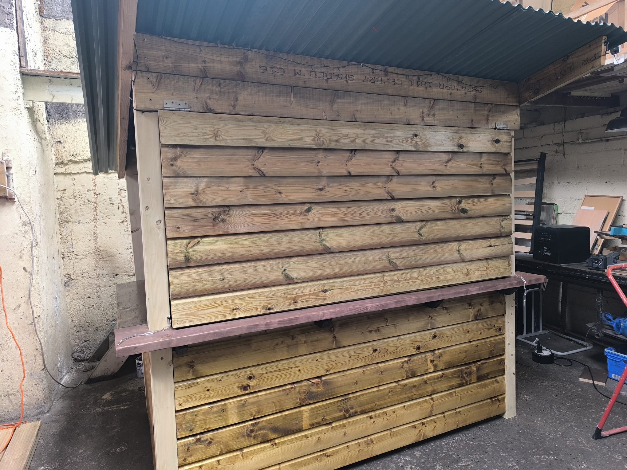 Rear view of a fully clad garden bar with a corrugated roof and a stained counter ledge