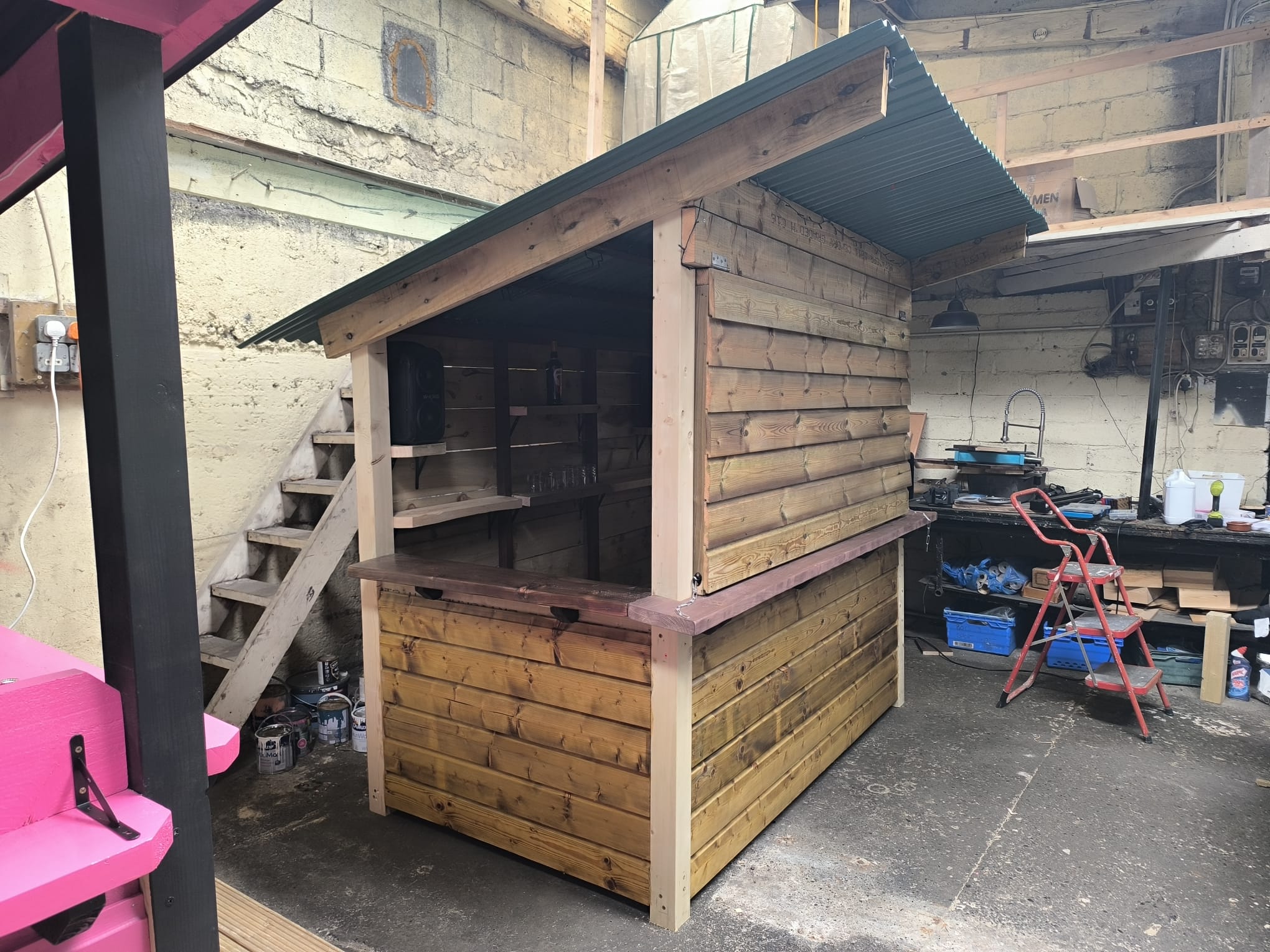 Corner garden bar with a corrugated roof, clad sides and an open serving corner